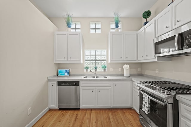 kitchen with light wood-type flooring, appliances with stainless steel finishes, a healthy amount of sunlight, and white cabinetry