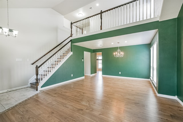 unfurnished living room with a notable chandelier, high vaulted ceiling, and wood-type flooring