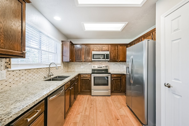 kitchen with appliances with stainless steel finishes, backsplash, sink, light wood-type flooring, and light stone countertops