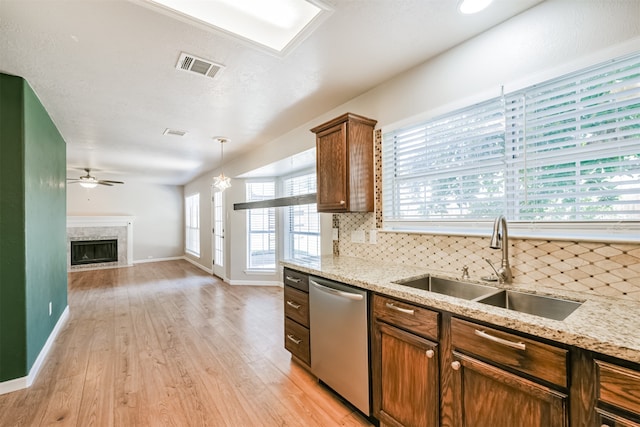 kitchen featuring stainless steel dishwasher, backsplash, light hardwood / wood-style flooring, sink, and a high end fireplace