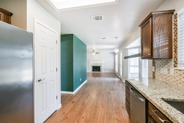 kitchen with light wood-type flooring, tasteful backsplash, light stone countertops, dishwasher, and decorative light fixtures