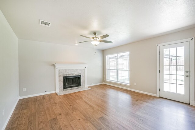 unfurnished living room with ceiling fan, a premium fireplace, and light hardwood / wood-style flooring