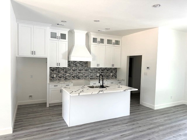 kitchen with custom exhaust hood, a kitchen island with sink, and white cabinetry