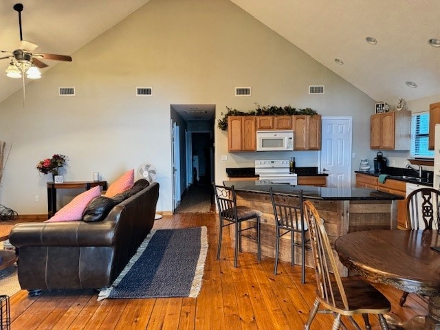 living room with ceiling fan, high vaulted ceiling, and light hardwood / wood-style floors