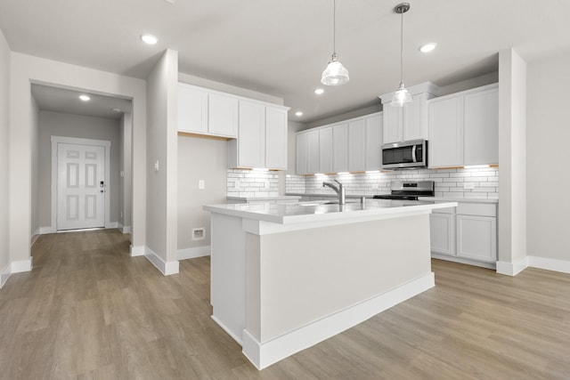 kitchen with a center island with sink, white cabinets, hanging light fixtures, decorative backsplash, and stainless steel appliances