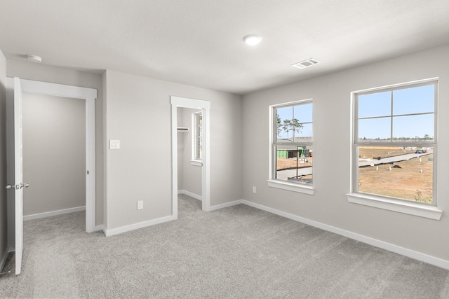 unfurnished bedroom featuring a spacious closet, a closet, and light colored carpet