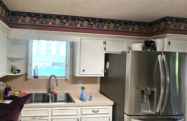 kitchen with sink, stainless steel fridge with ice dispenser, a textured ceiling, and white cabinetry