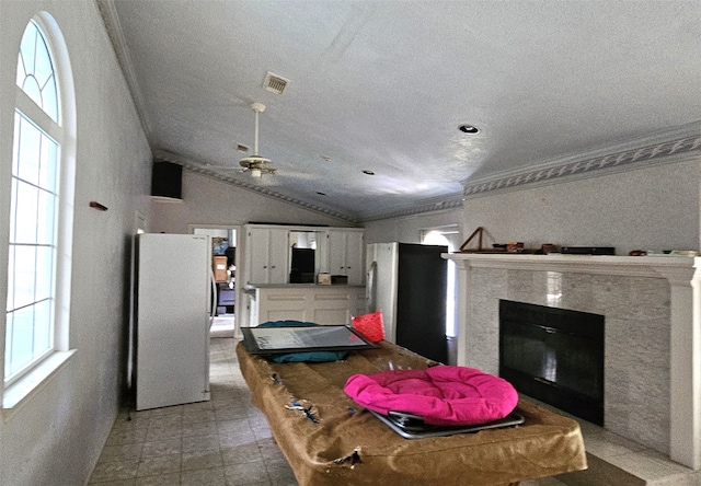 interior space featuring ceiling fan, vaulted ceiling, a tiled fireplace, stainless steel fridge, and light tile patterned flooring