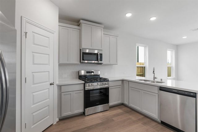 kitchen with sink, kitchen peninsula, appliances with stainless steel finishes, and wood-type flooring