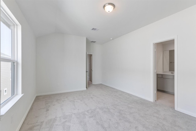 unfurnished bedroom with vaulted ceiling, ensuite bath, and light colored carpet