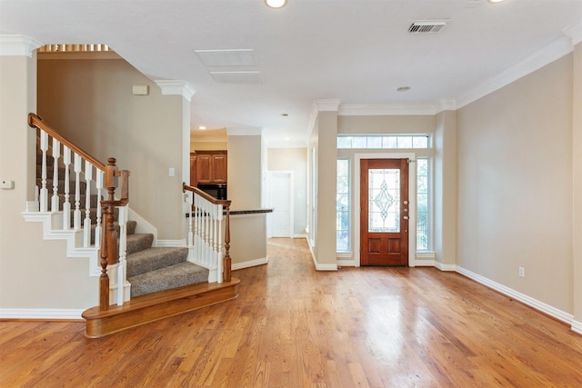 foyer entrance featuring visible vents, ornamental molding, light wood-type flooring, baseboards, and stairs