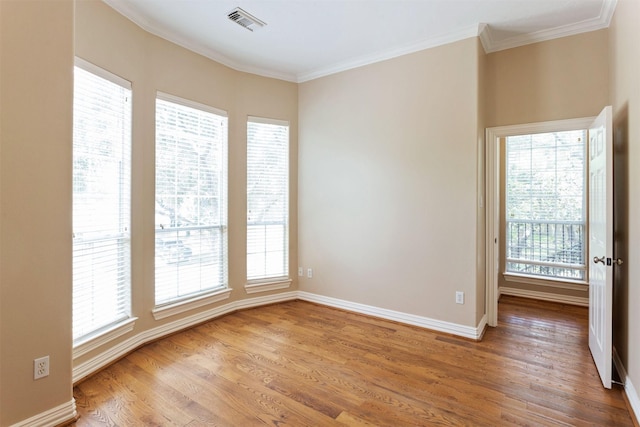 unfurnished room featuring baseboards, wood finished floors, visible vents, and crown molding