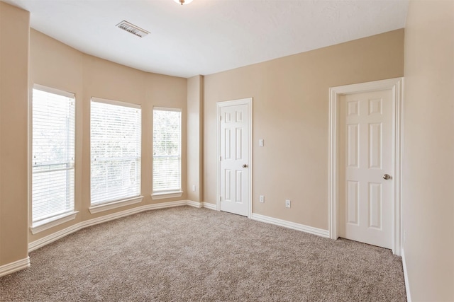 carpeted empty room with a healthy amount of sunlight, baseboards, and visible vents