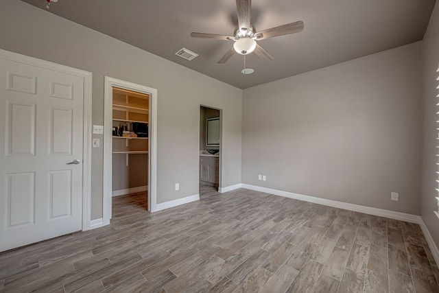 unfurnished bedroom featuring hardwood / wood-style floors, a spacious closet, a closet, ceiling fan, and ensuite bathroom