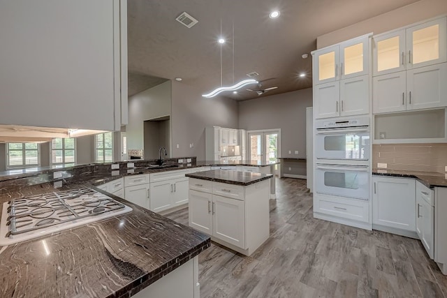 kitchen featuring white double oven, hanging light fixtures, dark stone countertops, kitchen peninsula, and a center island