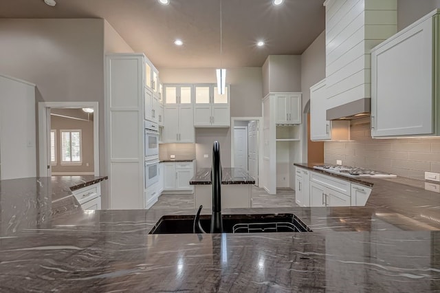 kitchen with sink, a high ceiling, decorative backsplash, pendant lighting, and white cabinets