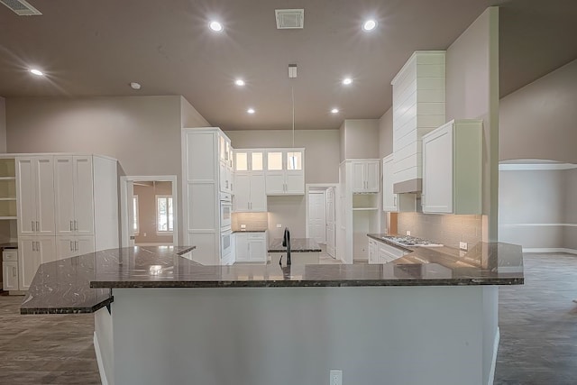 kitchen with hardwood / wood-style flooring, decorative backsplash, dark stone countertops, and white cabinetry