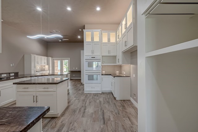 kitchen with white double oven, white cabinets, dark stone countertops, and hanging light fixtures