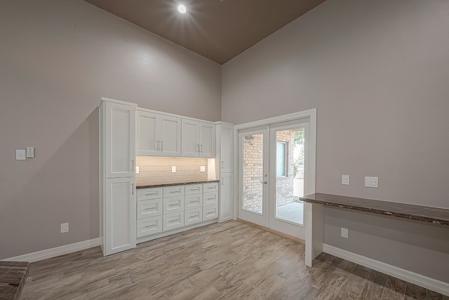 kitchen featuring dark stone counters, light hardwood / wood-style flooring, backsplash, high vaulted ceiling, and white cabinets