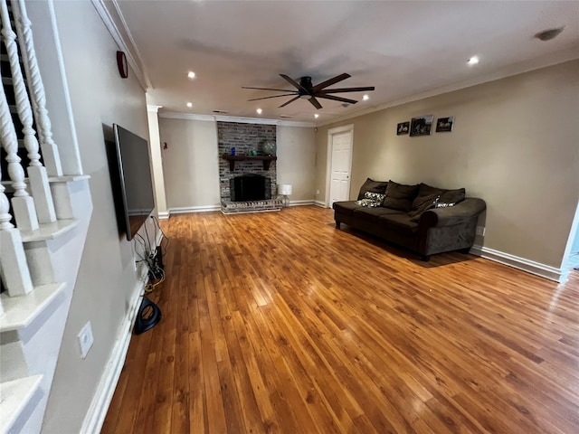 living room with hardwood / wood-style flooring, ceiling fan, crown molding, and a brick fireplace