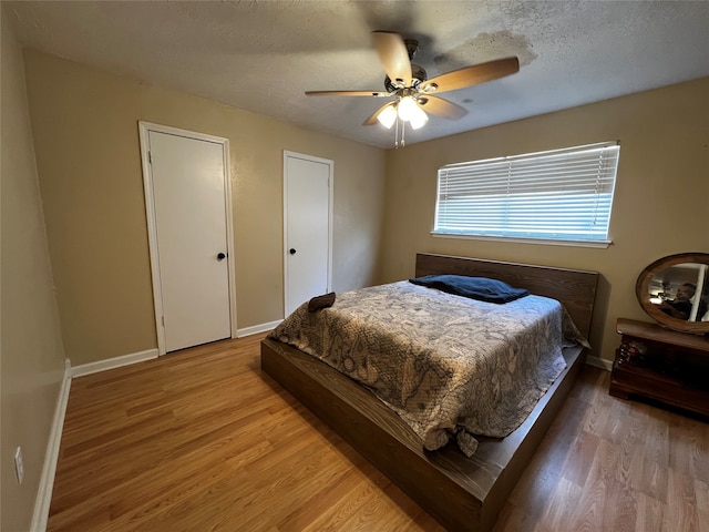 bedroom featuring multiple closets, ceiling fan, hardwood / wood-style floors, and a textured ceiling