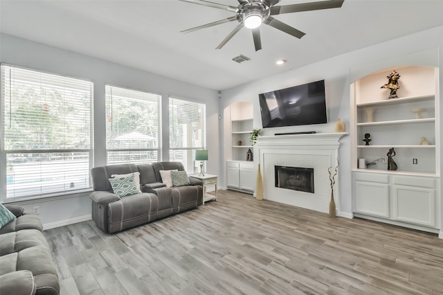 living room featuring a brick fireplace, a wealth of natural light, and light hardwood / wood-style floors