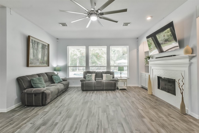 living room with ceiling fan, a fireplace, and light hardwood / wood-style floors