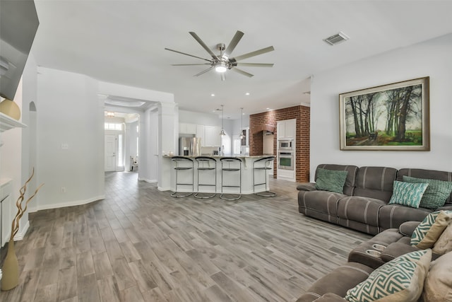 living room featuring ornate columns, light wood-type flooring, and ceiling fan