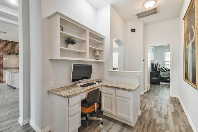 office area with brick wall, built in desk, and light hardwood / wood-style floors