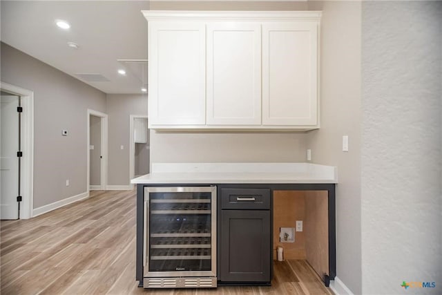 bar with wine cooler, light wood-type flooring, and white cabinets