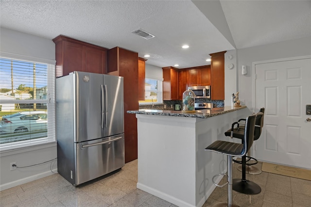 kitchen with dark stone countertops, tasteful backsplash, a kitchen bar, kitchen peninsula, and stainless steel appliances