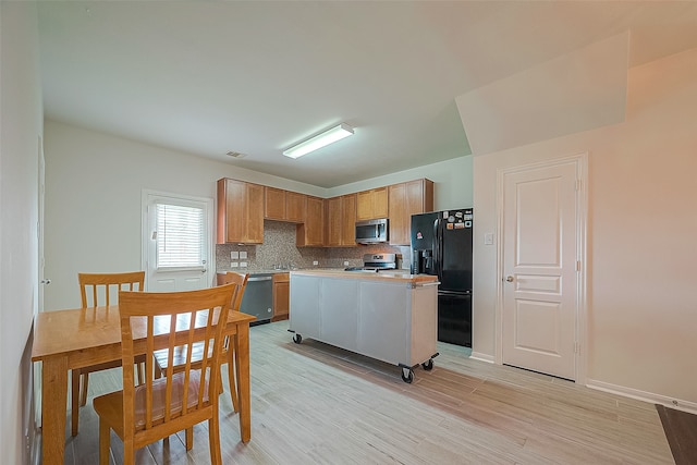 kitchen with light wood-type flooring, appliances with stainless steel finishes, decorative backsplash, and a kitchen island