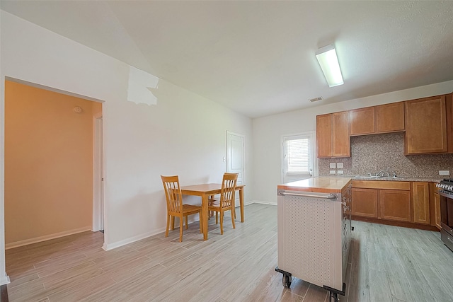 kitchen with light hardwood / wood-style flooring, sink, stainless steel gas stove, and decorative backsplash