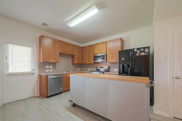 kitchen featuring wood counters, appliances with stainless steel finishes, a center island, light hardwood / wood-style floors, and decorative backsplash