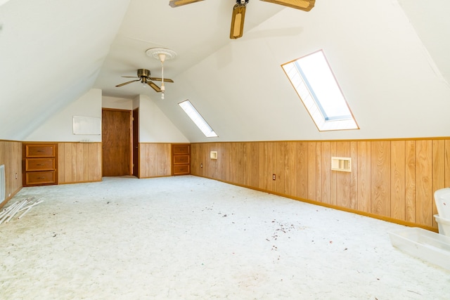 additional living space featuring ceiling fan, vaulted ceiling with skylight, and wood walls