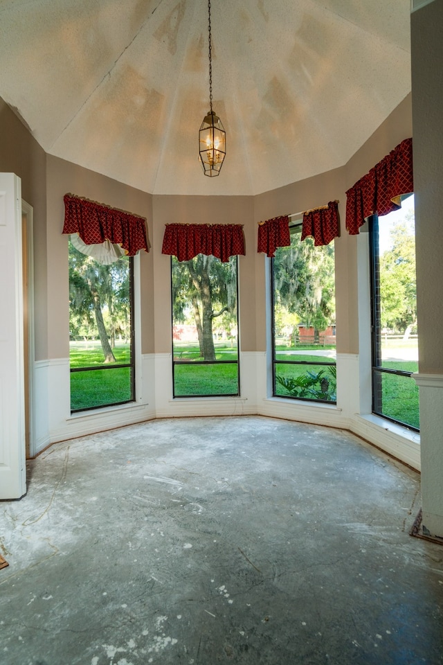 unfurnished living room featuring vaulted ceiling, a textured ceiling, a healthy amount of sunlight, and a chandelier