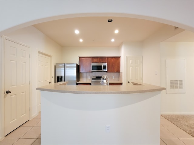 kitchen featuring a kitchen island with sink, light tile patterned floors, backsplash, and stainless steel appliances