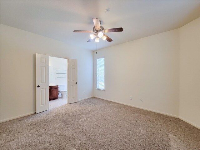 unfurnished bedroom featuring ceiling fan, light carpet, and ensuite bath