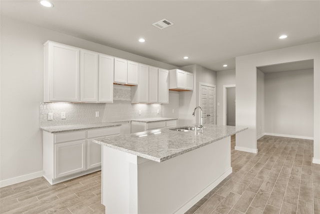 kitchen featuring white cabinets, light hardwood / wood-style floors, a center island with sink, and sink