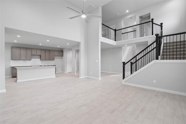 unfurnished living room featuring ceiling fan, sink, light hardwood / wood-style floors, and a towering ceiling