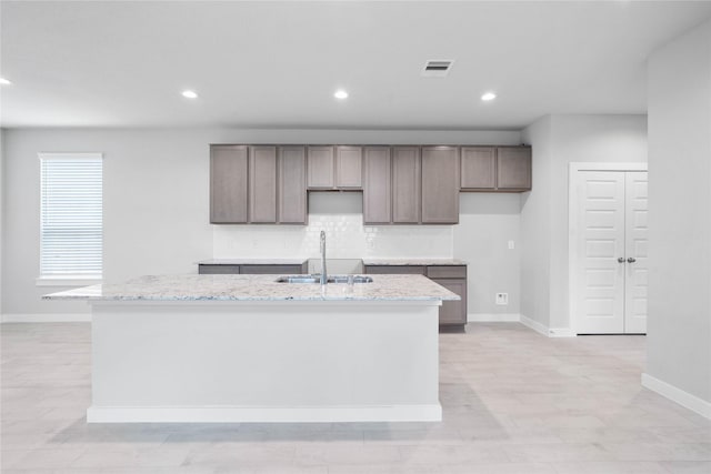 kitchen featuring tasteful backsplash, sink, light stone countertops, and a center island with sink