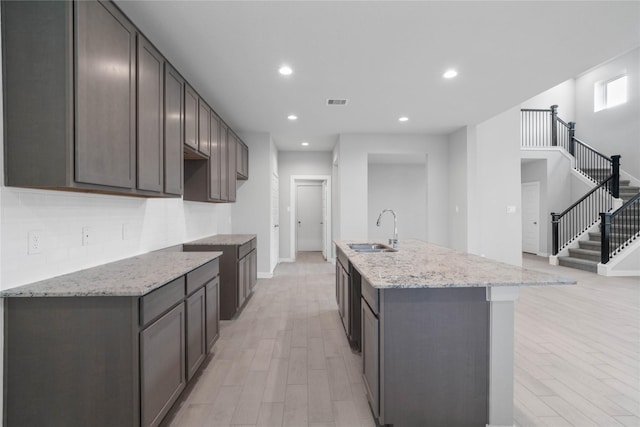 kitchen featuring sink, light wood-type flooring, light stone countertops, and a center island with sink