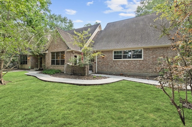 rear view of property featuring roof with shingles, a lawn, and brick siding