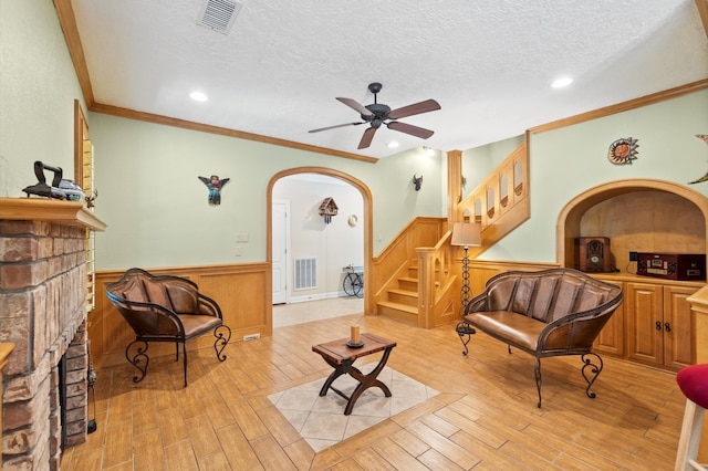 sitting room featuring light hardwood / wood-style flooring, crown molding, a fireplace, a textured ceiling, and ceiling fan