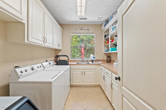 laundry area with cabinets, independent washer and dryer, light tile patterned floors, sink, and a textured ceiling