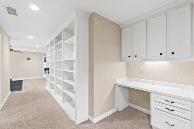 unfurnished office featuring ceiling fan, built in desk, and light colored carpet