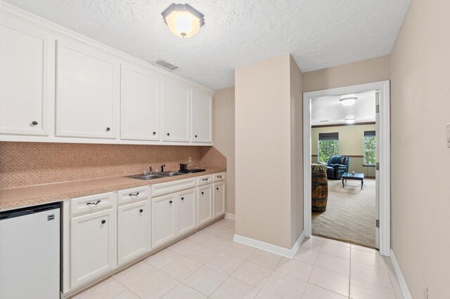 kitchen featuring sink, a textured ceiling, light carpet, refrigerator, and white cabinets