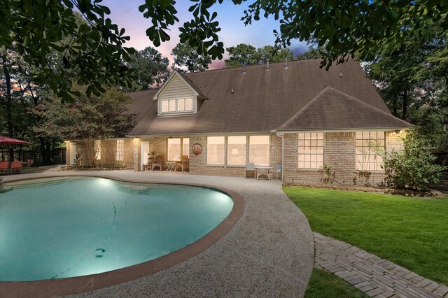 pool at dusk with a lawn and a patio area