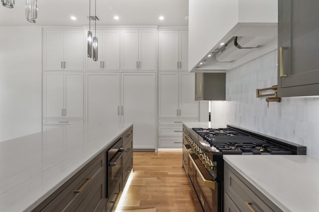 kitchen featuring light wood-type flooring, range with two ovens, white cabinetry, pendant lighting, and wall chimney range hood