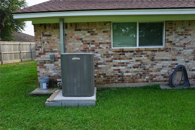 exterior details with fence, roof with shingles, central AC, and brick siding
